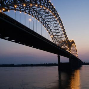 Arched suspension bridge with lights at sunset over a river