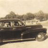 White man and woman in four-door car with service station in the background