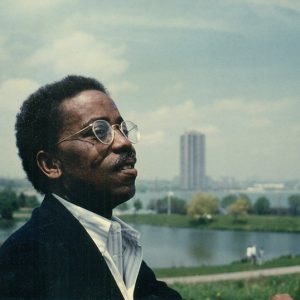 African-American man with glasses speaking with cityscape behind him