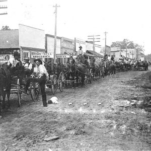 Men driving horse drawn wagons on town street