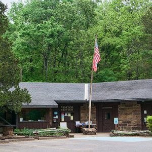 Wood and stone building with flagpole and parking lot with trees in background