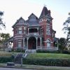 ornate multistory house with covered porch balcony and a tower with steps leading to the street