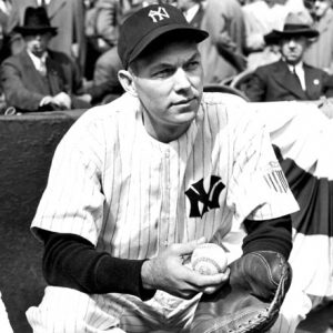 White man crouching in a New York Yankee uniform with ball and glove and spectators in background