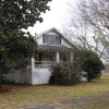 Small two-story white house with covered porch and trees