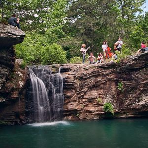 White men women and children standing on rock wall above waterfall and pool of water