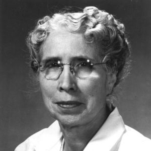 Old white woman with curly hair and glasses in white coat