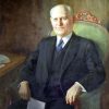 Old white man in suit with a blue tie sitting in a green chair