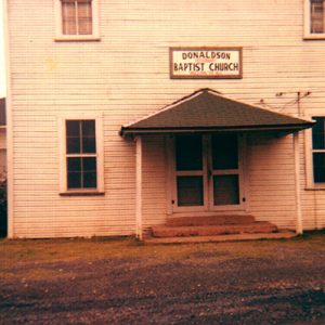 Multistory "Donaldson Baptist Church" building with covered porch and single-story extension on grass