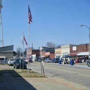 Street with brick storefronts flag poles parked cars and water tower