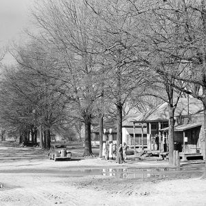 Car gas station storefronts and trees on dirt road