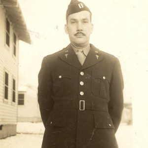 man with dark mustache standing in military uniform with cap