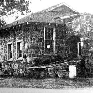 Single-story stone building with Dutch gable roof and arched entrance way