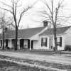 Single-story white house with covered porch with columns and driveway and bare trees in front