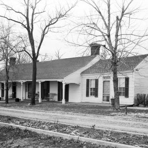 Single-story white house with covered porch with columns and driveway and bare trees in front