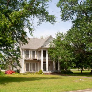 Two-story wooden house with columns amidst trees