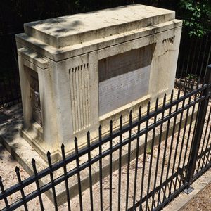 Stone monument with engraved plaque inside iron fence