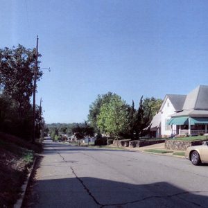 House with white siding and covered corner porch and gold car on street in residential neighborhood