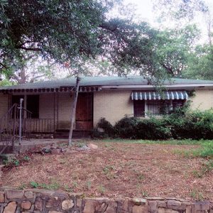 Steps with railing and sidewalk leading to single-story brick house with covered porch under tree