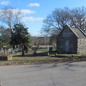 Brick mausoleum in cemetery with paved road in the foreground