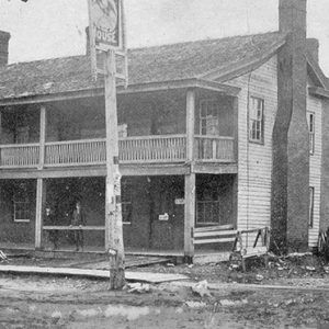 Two-story hotel with covered porch and balcony on dirt road