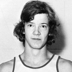 Young white man with curly hair in sleeveless "Arkansas" shirt featuring caricature of Native American