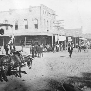 Multistory brick buildings with crowd walking on covered walkways on dirt road