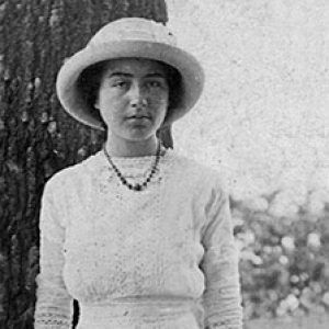 Young white woman in hat and dress standing next to a tree