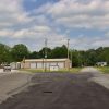 Street intersection with cars and metal garage building with outbuilding and radio tower in background