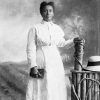 African-American woman in dress posing with hat on fence beside her