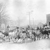 Crowded street with horse drawn wagons and white men in hats