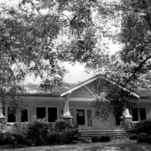 Front view of house with covered porch under large tree on street