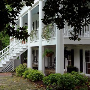 Side view of multistory house with covered porch and balcony as seen from under trees