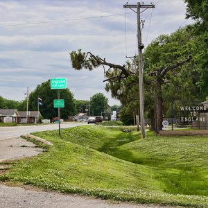 Green "England" road sign and "Welcome to England" sign on right side of highway with buildings in the background