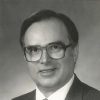 White man with glasses smiling in suit and tie