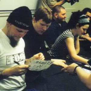 White men and woman seated at table signing autographs