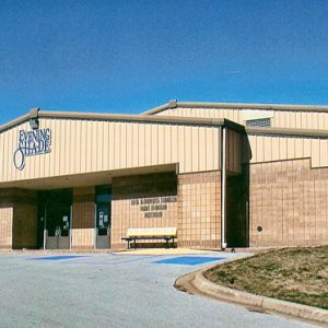 Brick building with metal roof and "Evening Shade" above the entrance with parking lot