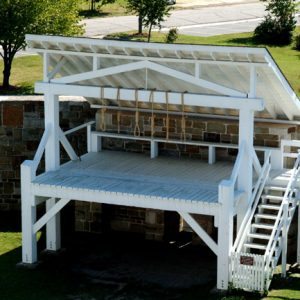 Covered wooden gallows with steps and raised walkway inside courtyard behind wooden and stone walls