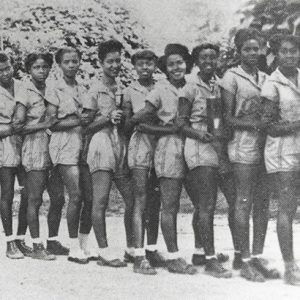 African-American girls in matching basketball uniforms with shorts standing in line with African-American woman in skirt