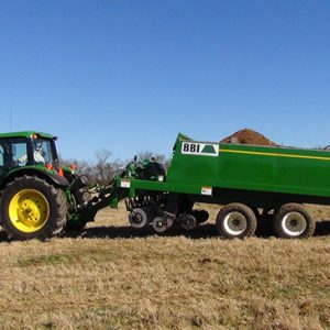 Green and yellow tractor pulling trailer loaded with soil in field