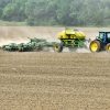 Green tractor pulling planter and tiller trailers in field