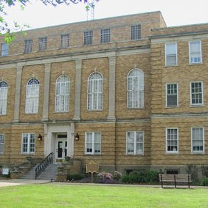 Multistory brick building with arched windows and historical marker sign on grass