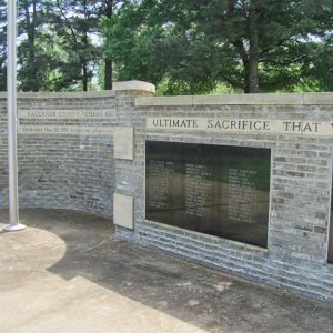 Brick memorial wall and flag pole with trees behind it