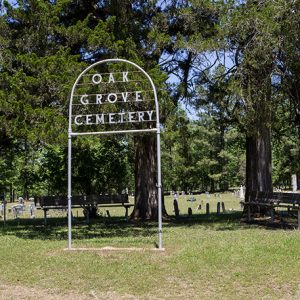 Iron arch sign and benches with tree outside cemetery