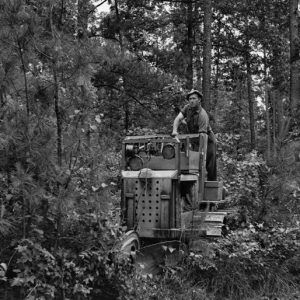 White man in hat using plow machine in forest