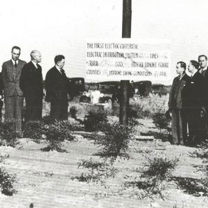 Groups of white men in suits on either side of sign on pole