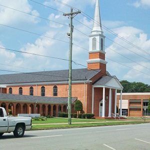 White truck driving down street past brick building with steeple and covered walkway