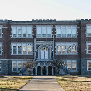 Three-story brick school building with arched entrance and stairs