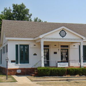 Single-story white building with two columns on porch and two sets of doors and windows