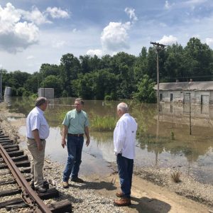 Three white men standing by railroad tracks observing flooded depot facility