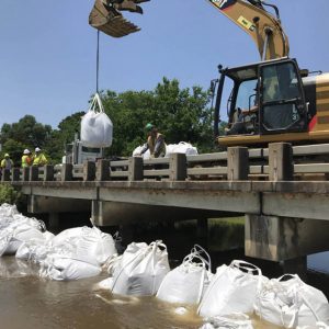 Sandbags being lowered off of a concrete bridge by an excavator to prevent flooding